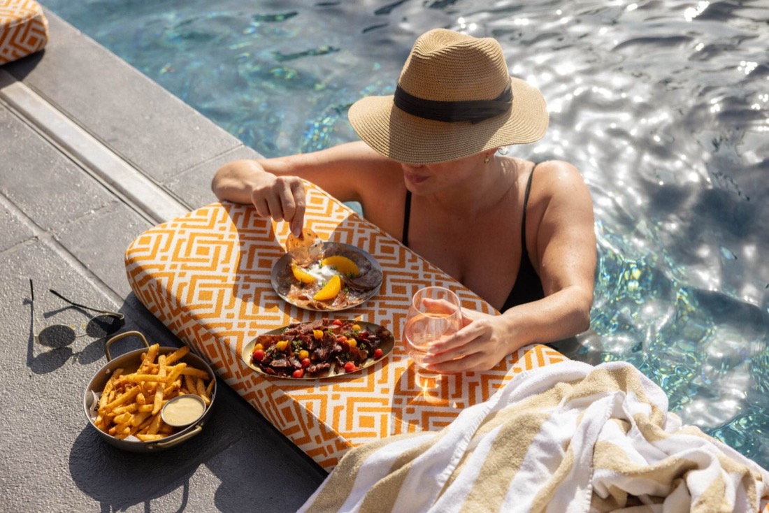 A guest in the rooftop pool at Above, Ovolo The Valley, food and rose on the poolside ledge