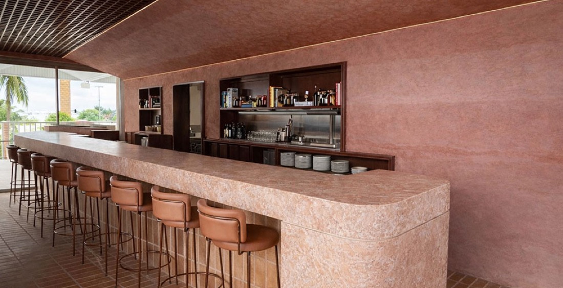 The rammed-earth bar at Ruma Rooftop, New Farm, terracotta walls and palms through the open side