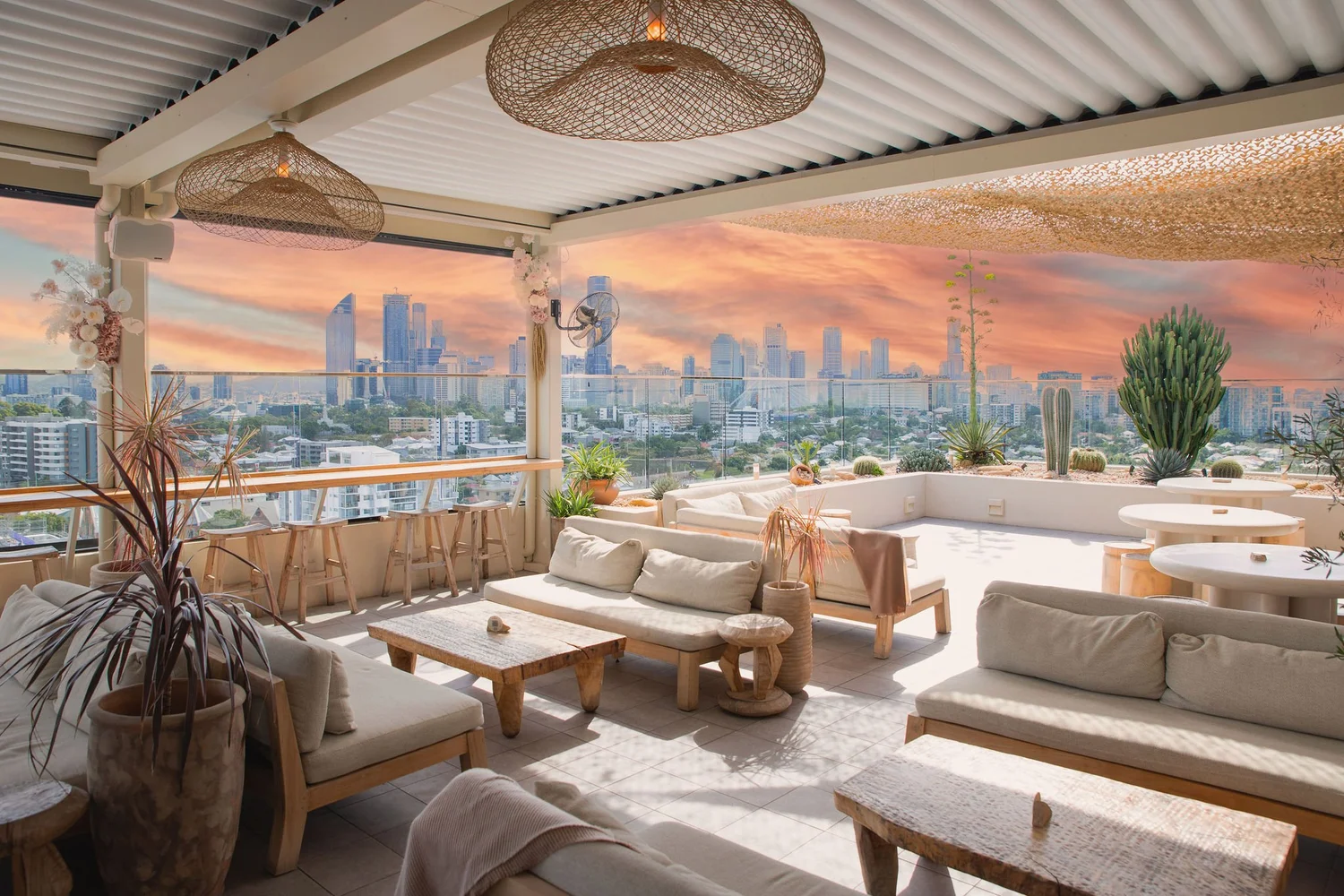 Sunsets Rooftop at Kangaroo Point, cream lounges and cactus under a pink sky over the Brisbane skyline
